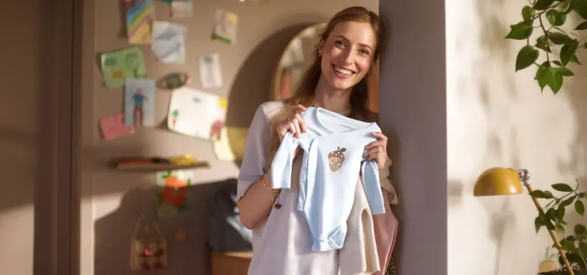 Glad mamma visar upp en ljusblå babybody med ett gulligt ekollonmotiv. Hon är veckans babe och ser fram emot att klä sin lilla skatt.