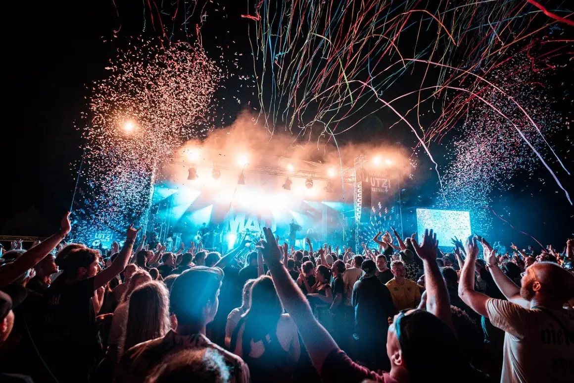 Konfetti regnet auf ein jubelndes Publikum bei einem Festival. Die Bühne ist hell beleuchtet, die Stimmung ist ausgelassen: ab geht die Lutzi!