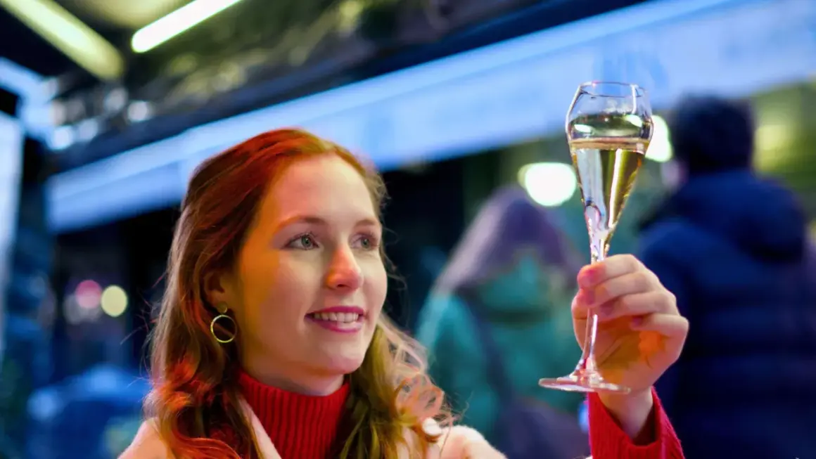 Frau mit roten Haaren hebt ein Glas Sekt, das auf der Hefe gereift ist, in festlicher Beleuchtung.