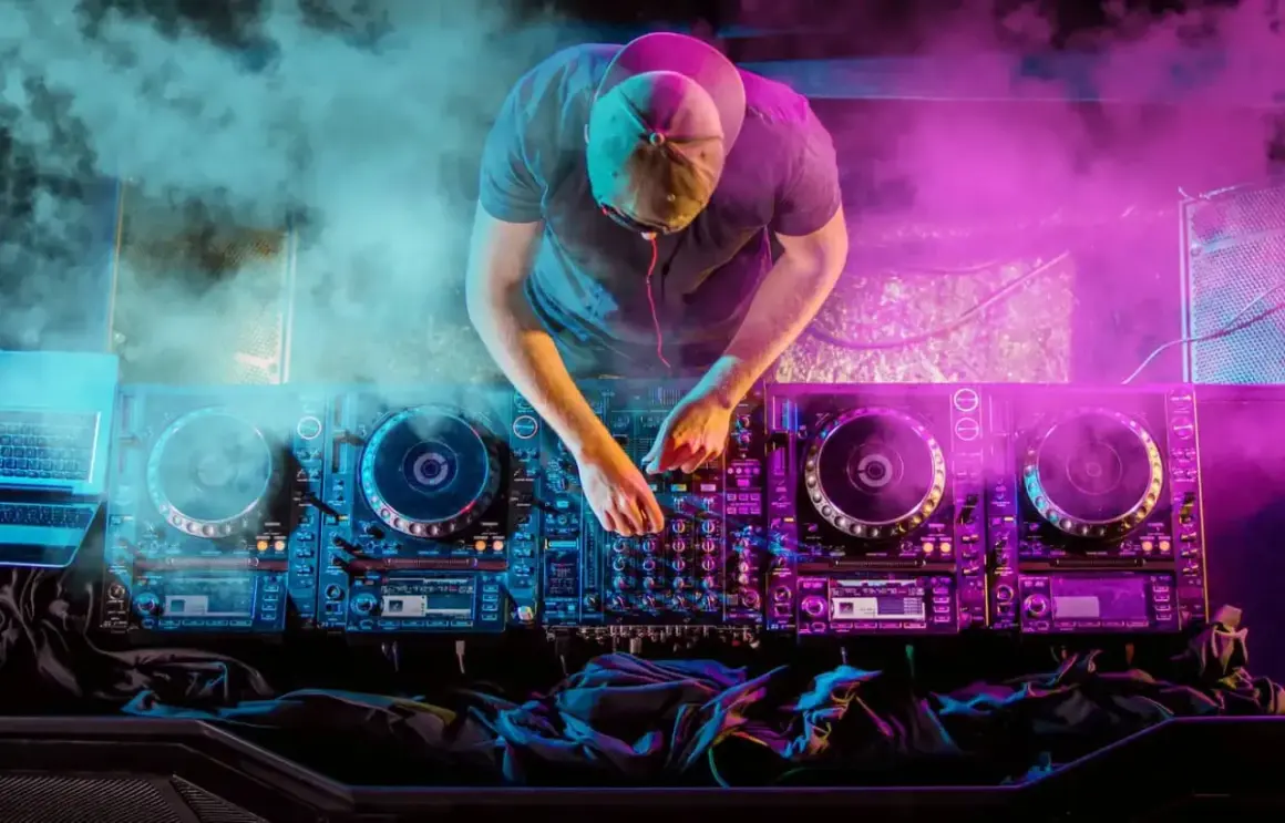 DJ con mani sui piatti, luci al neon e fumo creano l'atmosfera perfetta per la musica house famosa.