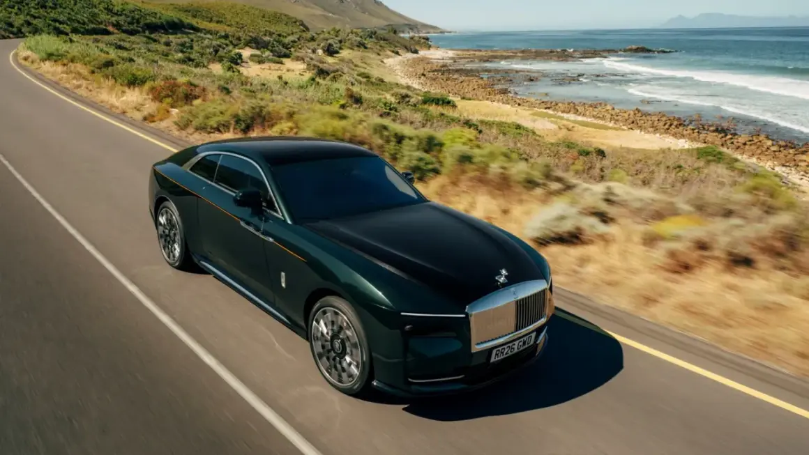 Elegancki, zielony Rolls Royce elektryczny sunie po malowniczej drodze nad oceanem.
