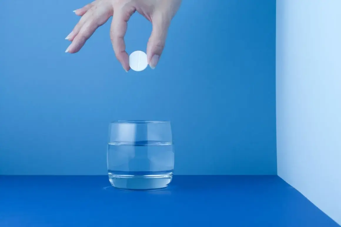 Mano deja caer una pastilla blanca, como un micropur, en un vaso de agua.