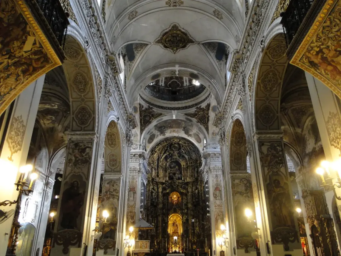 Interior de la iglesia de la Magdalena, con bóvedas ornamentadas, arcos y un retablo dorado.