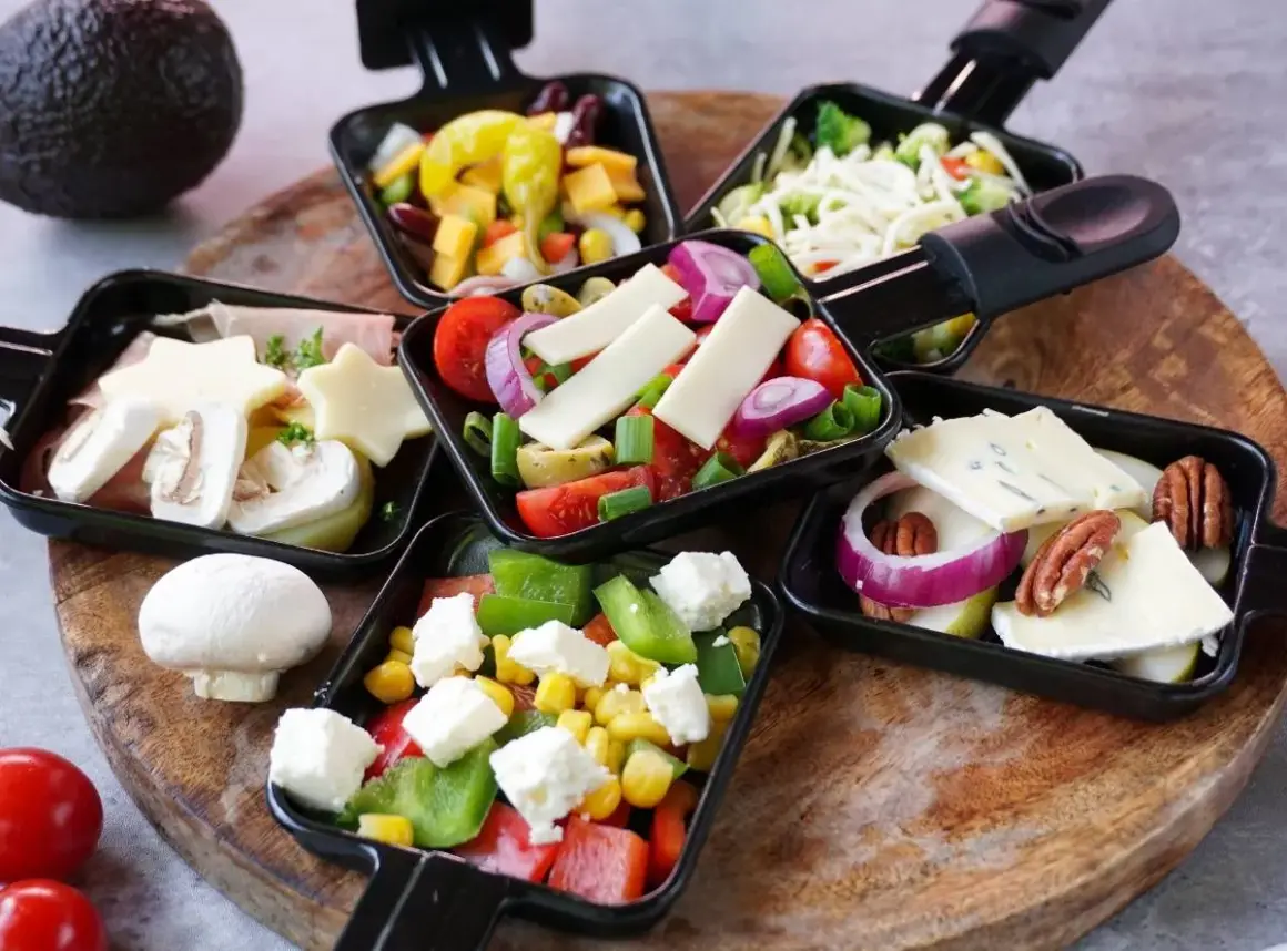 Raclette-Pfännchen mit Käse, Gemüse und Pilzen. Dazu passt ein kühler Weißwein oder ein Bier.