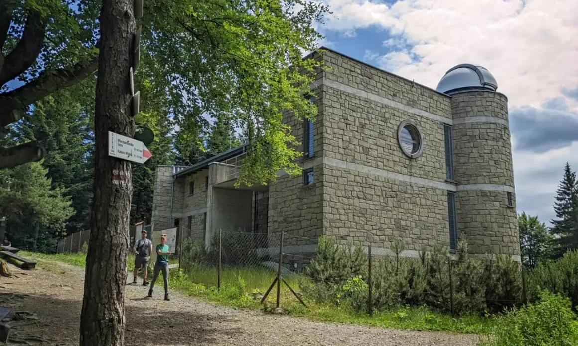 Kamienny budynek obserwatorium astronomicznego na szczycie góry. Obok tabliczka szlaku turystycznego PTTK.