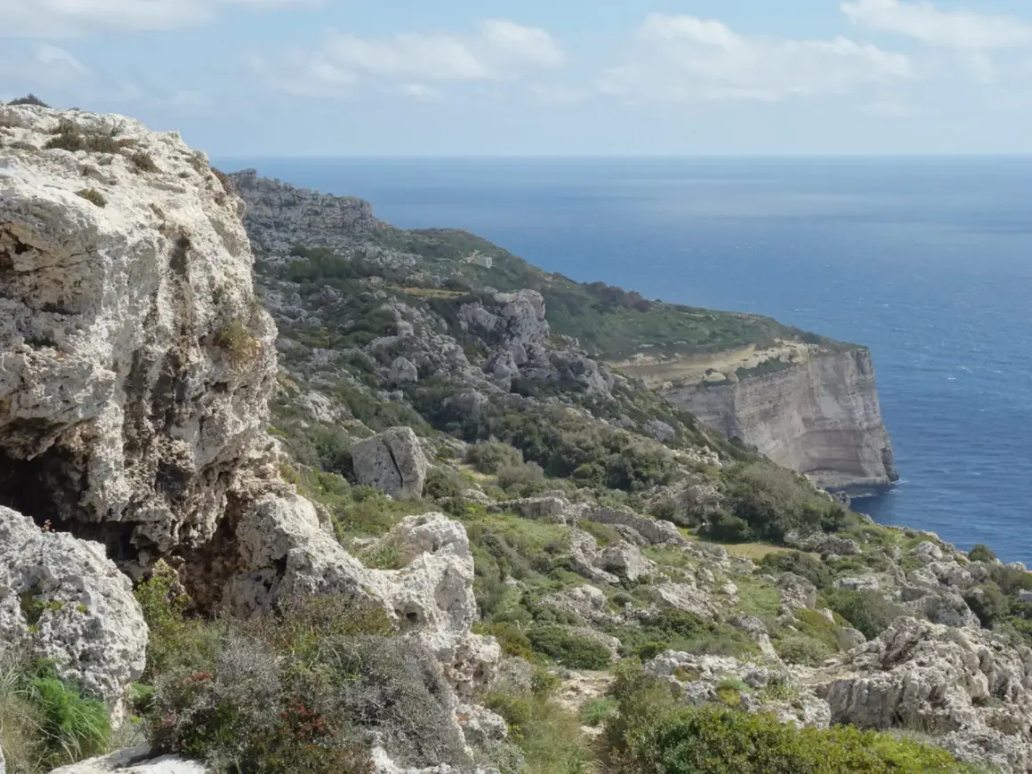 Malta's dramatic Dingli Cliffs, a rugged coastline meeting the deep blue sea under a cloudy sky.