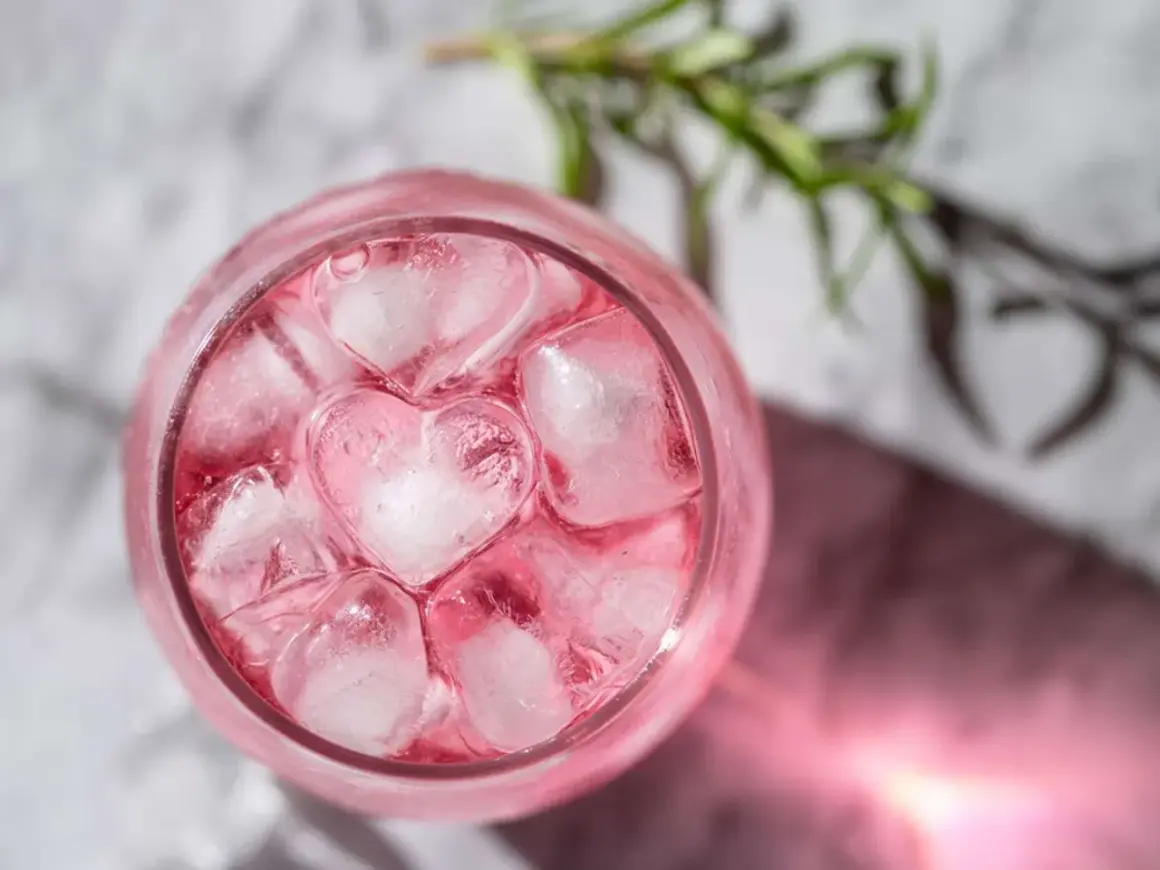 En rosa drink med hjärtformade isbitar och en rosmarinkvist.