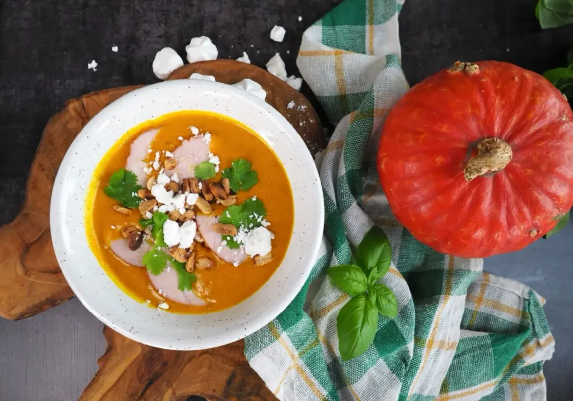Pomarańczowa zupa dyniowa z mięsem, serem feta, orzeszkami i kolendrą, obok dynia.