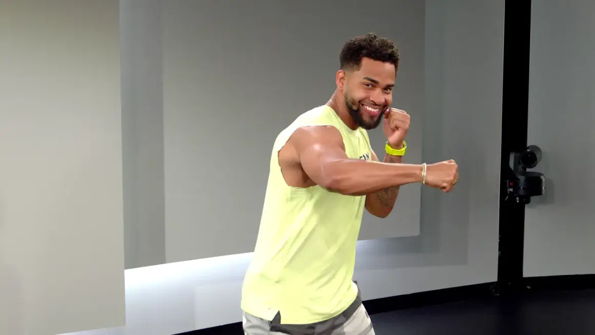 A smiling man in a yellow tank top throws a side hook punch, ready for his next workout move.