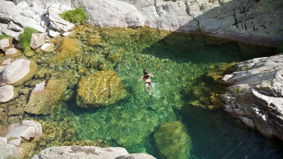 Una persona nada en pozas naturales de agua cristalina en la sierra de Madrid, rodeada de rocas y vegetación.