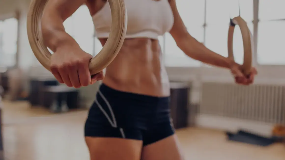 Kobieta z wyrzeźbionym brzuchem ćwiczy na kółkach gimnastycznych, przygotowując się do wyzwań crossfitu.