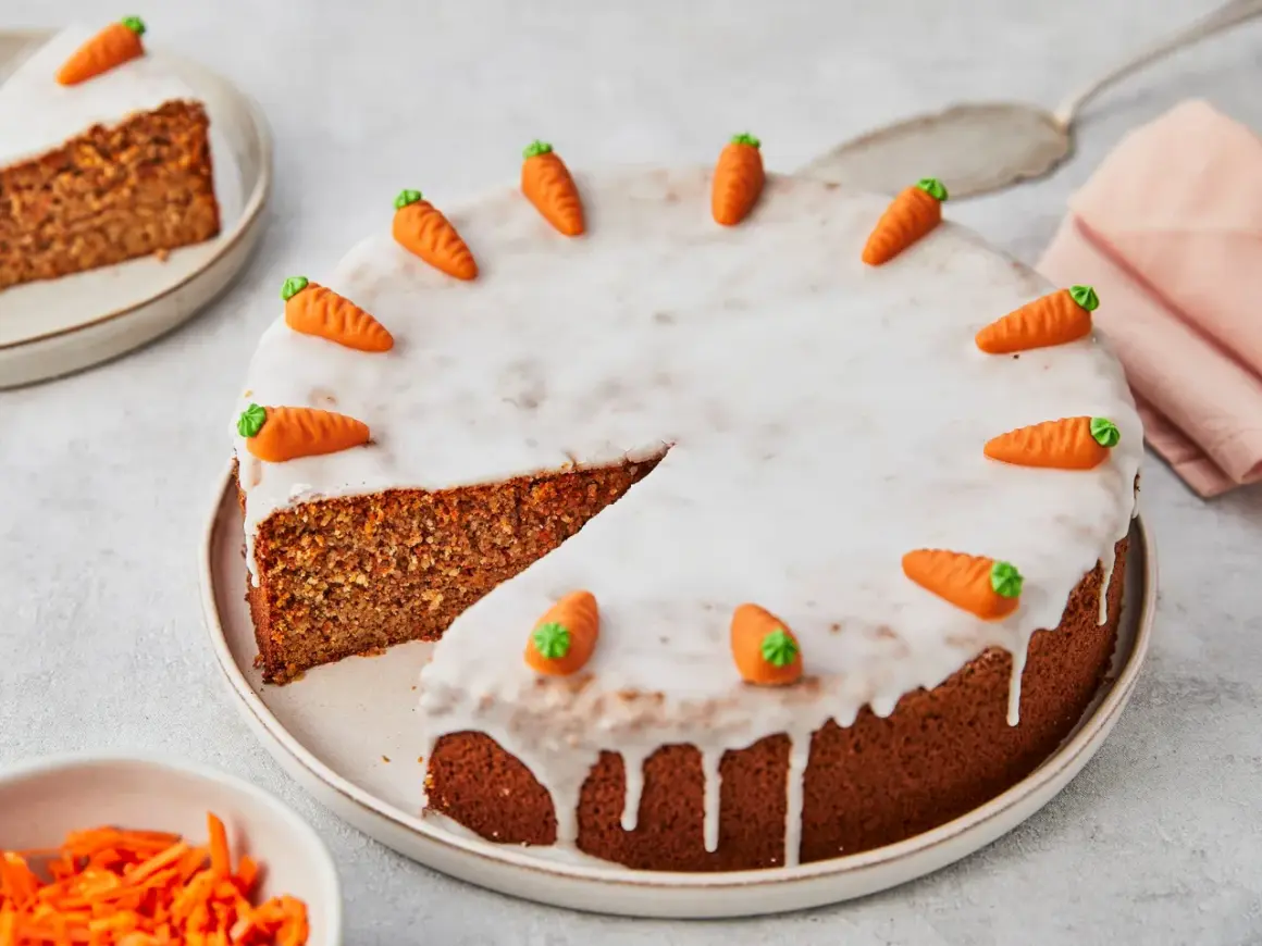 Ein saftiger karottenkuchen ohne mehl, verziert mit kleinen Marzipan-Karotten und Zuckerguss. Ein Stück ist bereits angeschnitten.