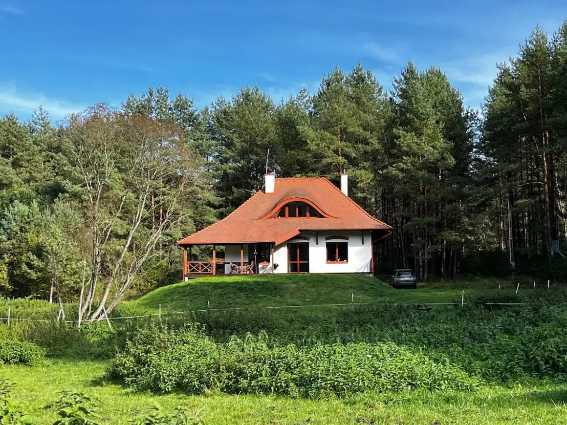 Urokliwy domek na wzgórzu pośród baśniowego boru. Otoczony zielenią, z czerwoną, spadzistą dachem i werandą.