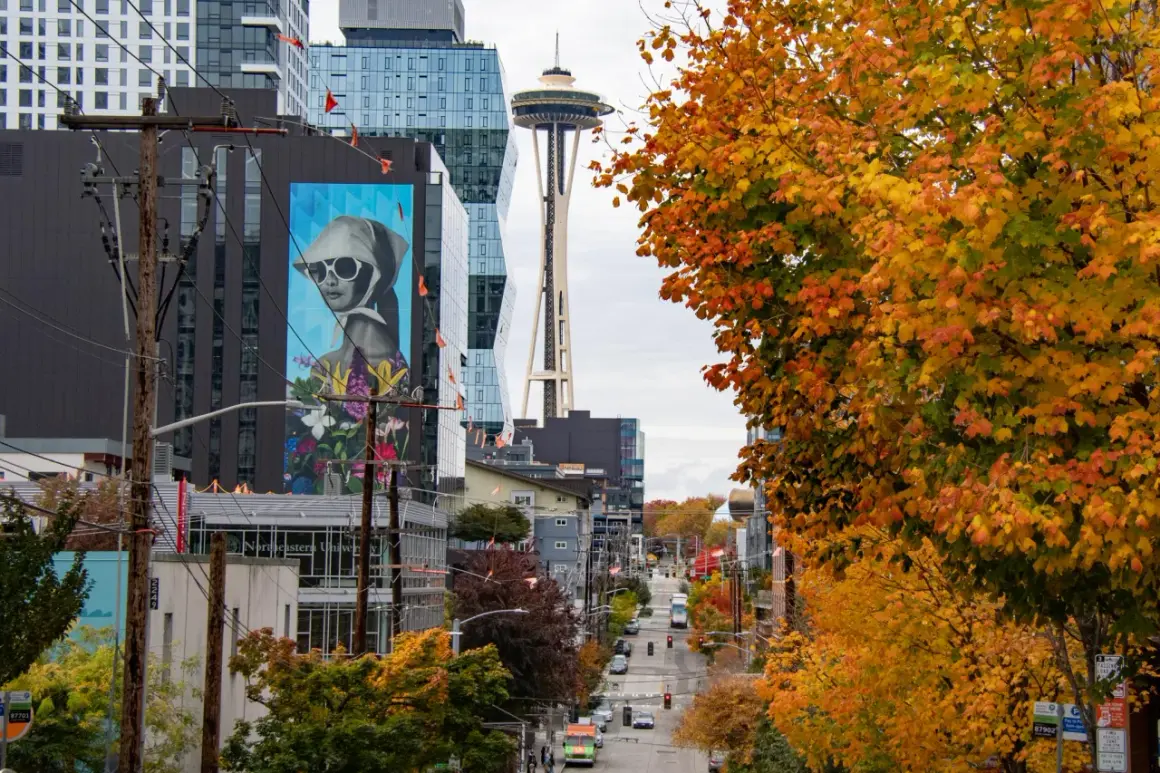 Seattle street photography captures a vibrant autumn scene with colorful trees, a mural, and the Space Needle in the distance.