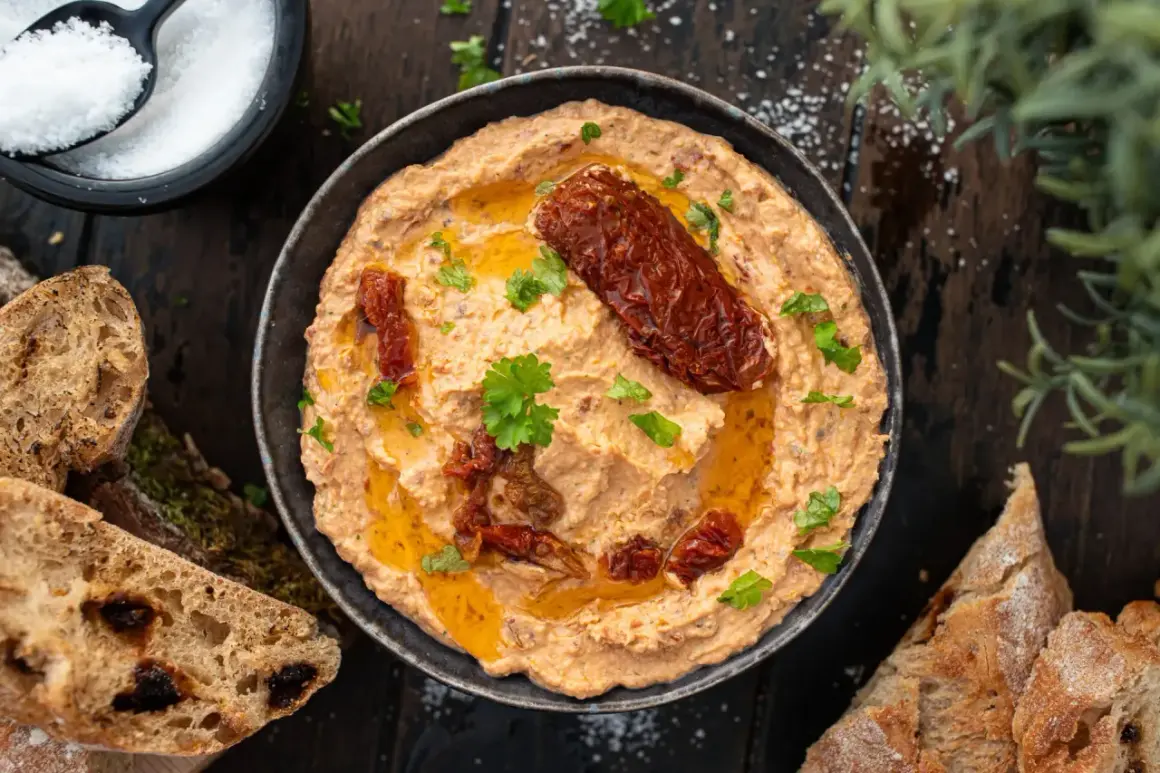 Cremiger Feta Dip mit sonnengetrockneten Tomaten, Olivenöl und frischer Petersilie, serviert mit knusprigem Brot.