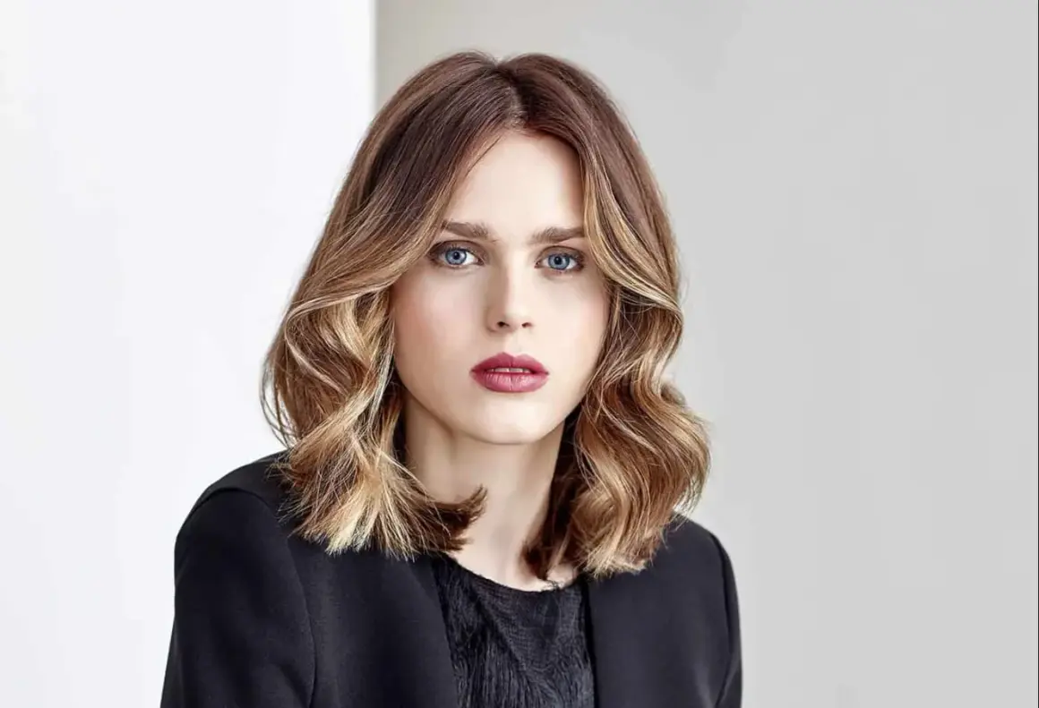 Une femme au regard intense, ses cheveux mi-longs aux reflets blonds et châtains, un parfait exemple de *ombre hair contouring*.