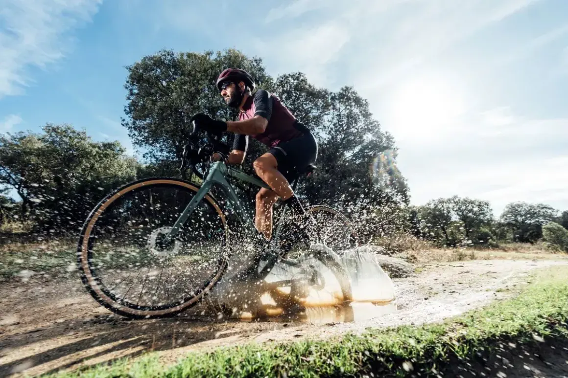 Ciclista en bici de gravel salpicando agua en un camino rural. ¡Así es el gravel!