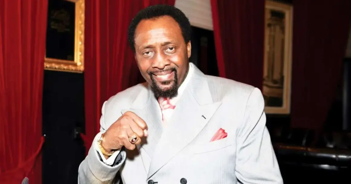 Thomas Hearns now, a boxing legend, smiles confidently in a light grey suit, red tie, and pocket square.