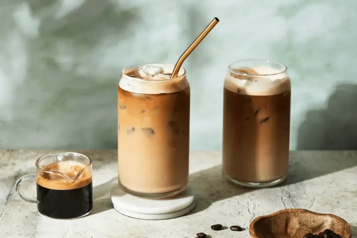 Deux verres de latte froid avec une paille dorée, un petit shot d'espresso et des grains de café.