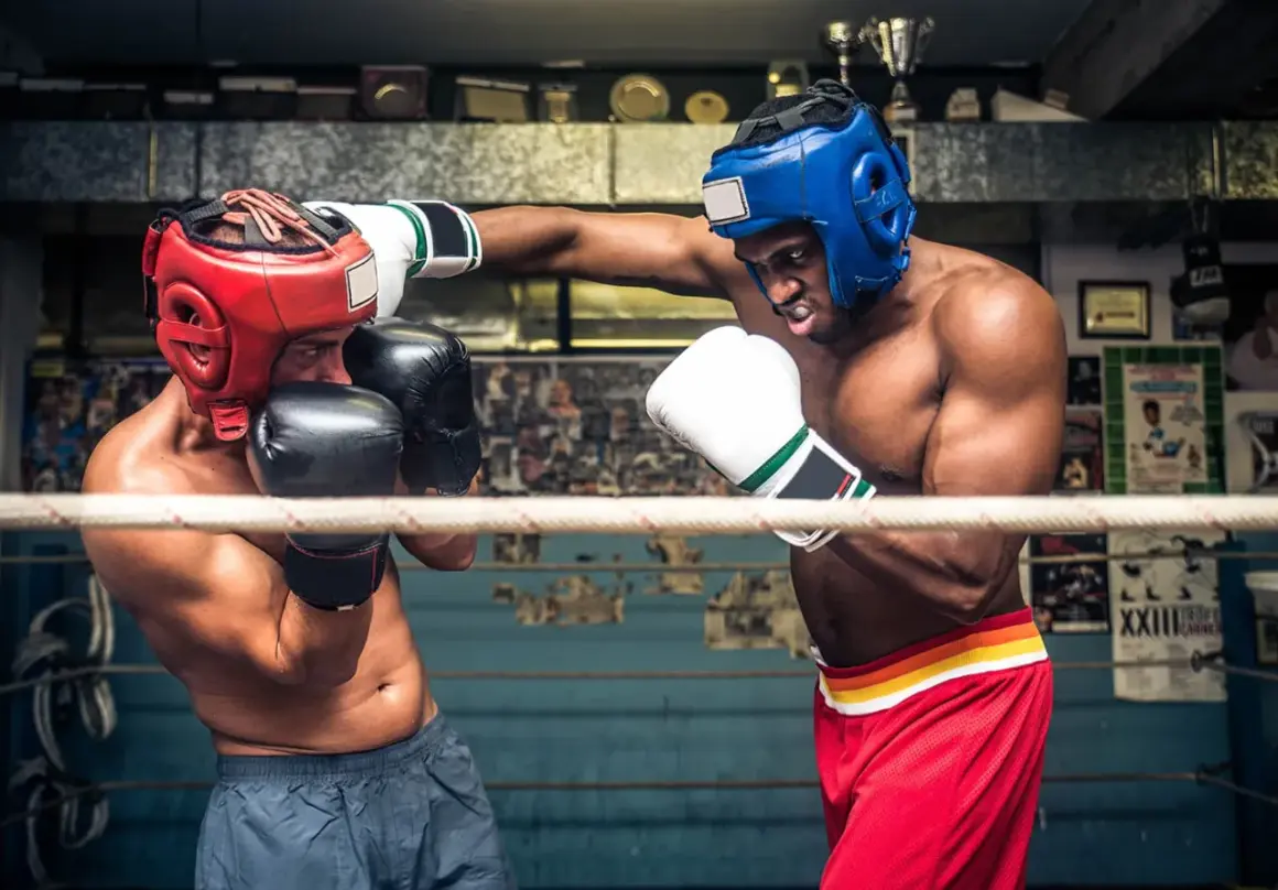 Två boxare i ringen, en med röd och en med blå hjälm, tränar funktionell fitness.