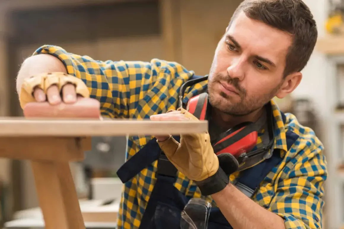 Artisan méticuleux, il s'applique à raboter une porte en bois avec soin.