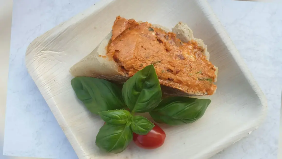 Ein Stück Brot mit leckerer Tomatenbutter, garniert mit frischem Basilikum und einer Kirschtomate. Perfekt zum Tomatenbutter selber machen.