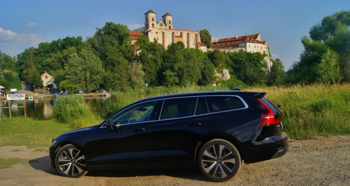 Czarne Volvo V60 na tle malowniczego klasztoru i rzeki. Idealne na wakacyjne podróże, gdzie niskie volvo v60 spalanie pozwoli cieszyć się widokami.