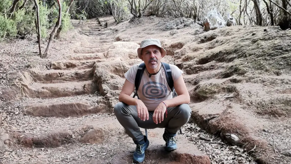Hombre con sombrero y mochila en el sendero de los sentidos Tenerife, rodeado de vegetación y escalones de tierra.