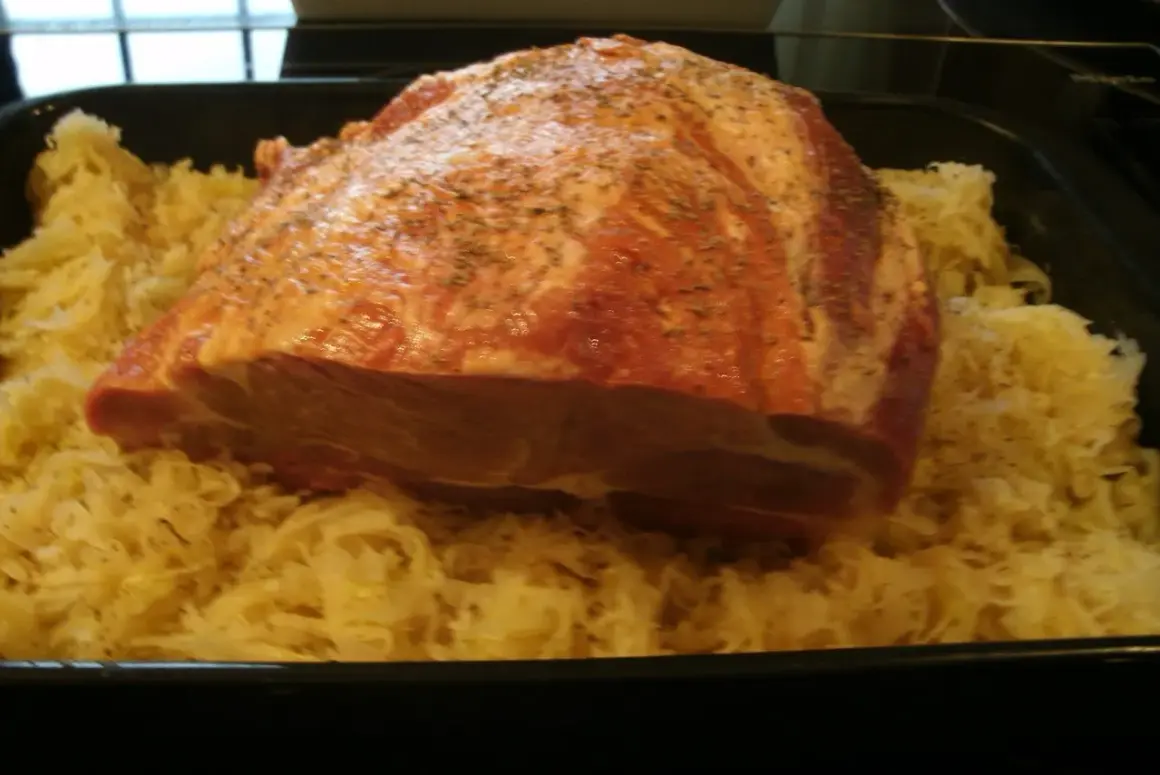 Rohes Schweinefleisch mit Gewürzen liegt auf Sauerkraut in einer Bratreine. Bereit zum Kochen.