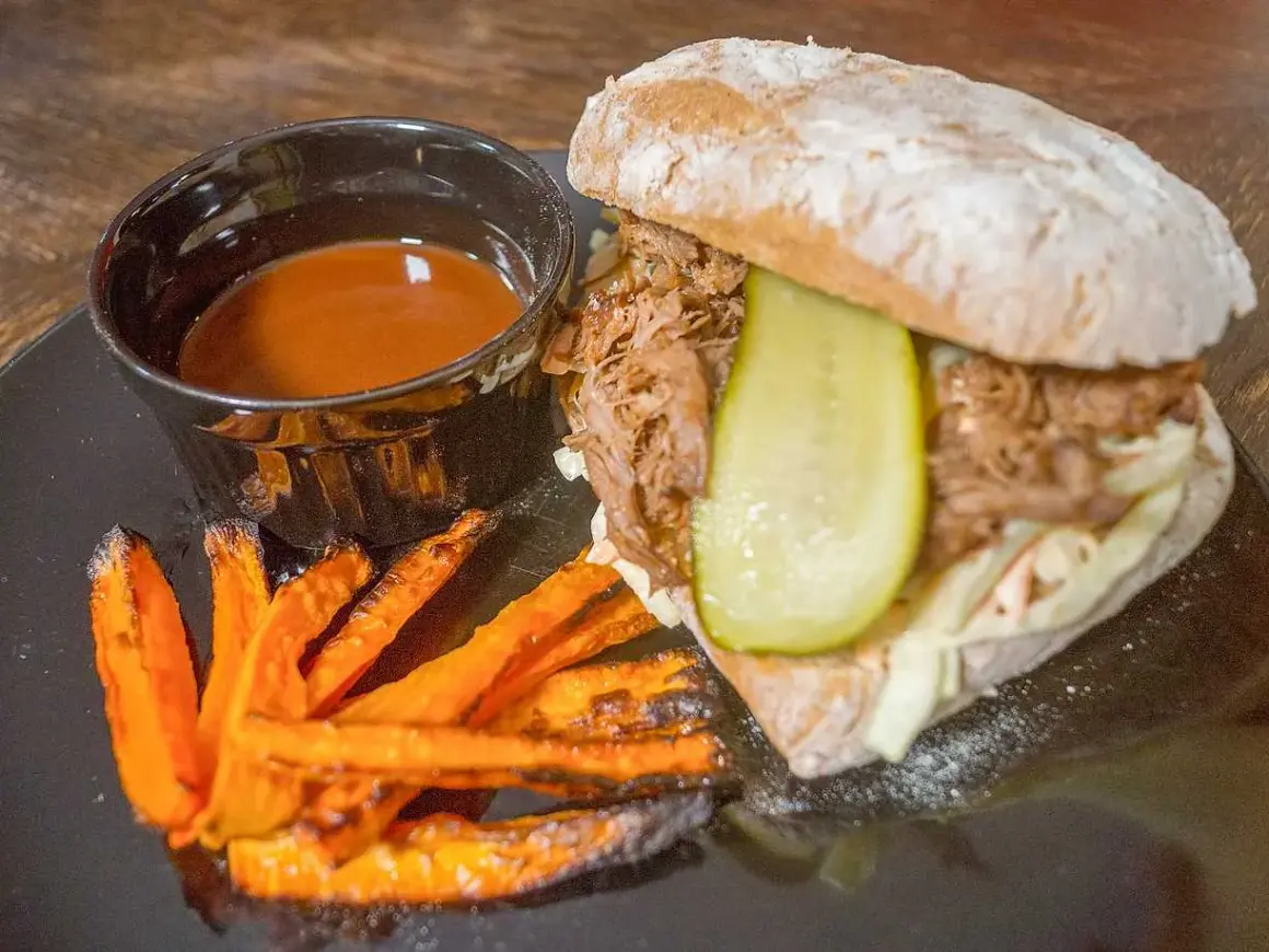 Pulled pork-macka med krispiga sötpotatispommes och en skål med smakrik sås till pulled pork.