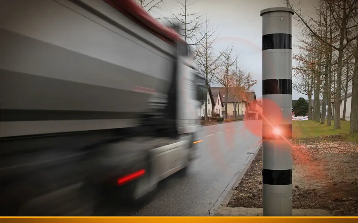 Ein Lkw rast an einem Blitzer vorbei. Der Blitz leuchtet auf, als der Fahrer zu schnell fährt.