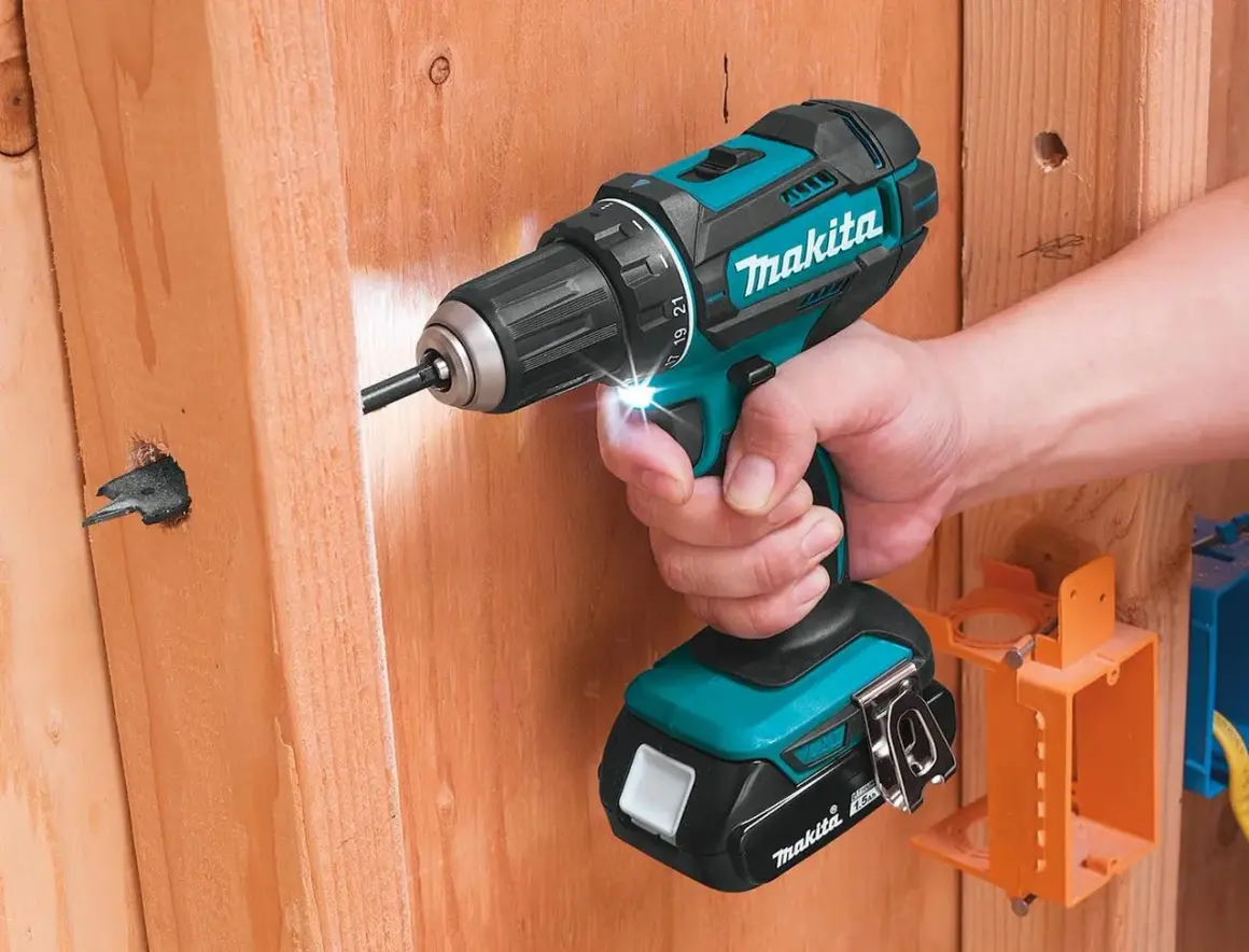 Une perceuse Makita d'origine, tenue par une main, perce un trou dans du bois. L'outil est puissant et fiable.