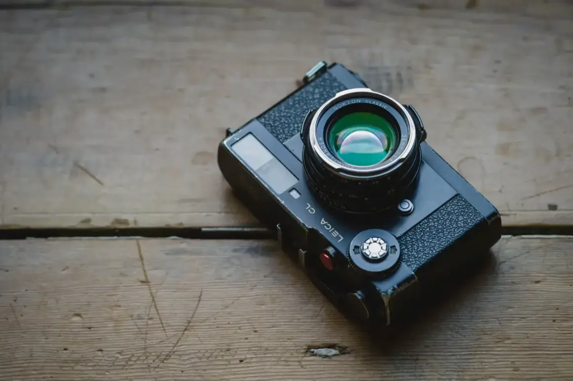 A Leica CL camera with a Nokton Classic lens rests on a weathered wooden surface, ready for a detailed review.
