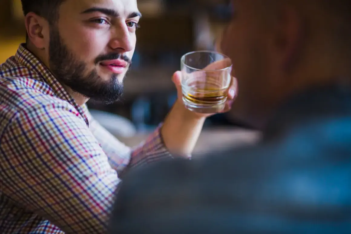 Mężczyzna z zarostem, w kratę, trzymający szklankę z bursztynowym płynem. W jego oczach widać pustkę, typową dla narcyza alkoholika.