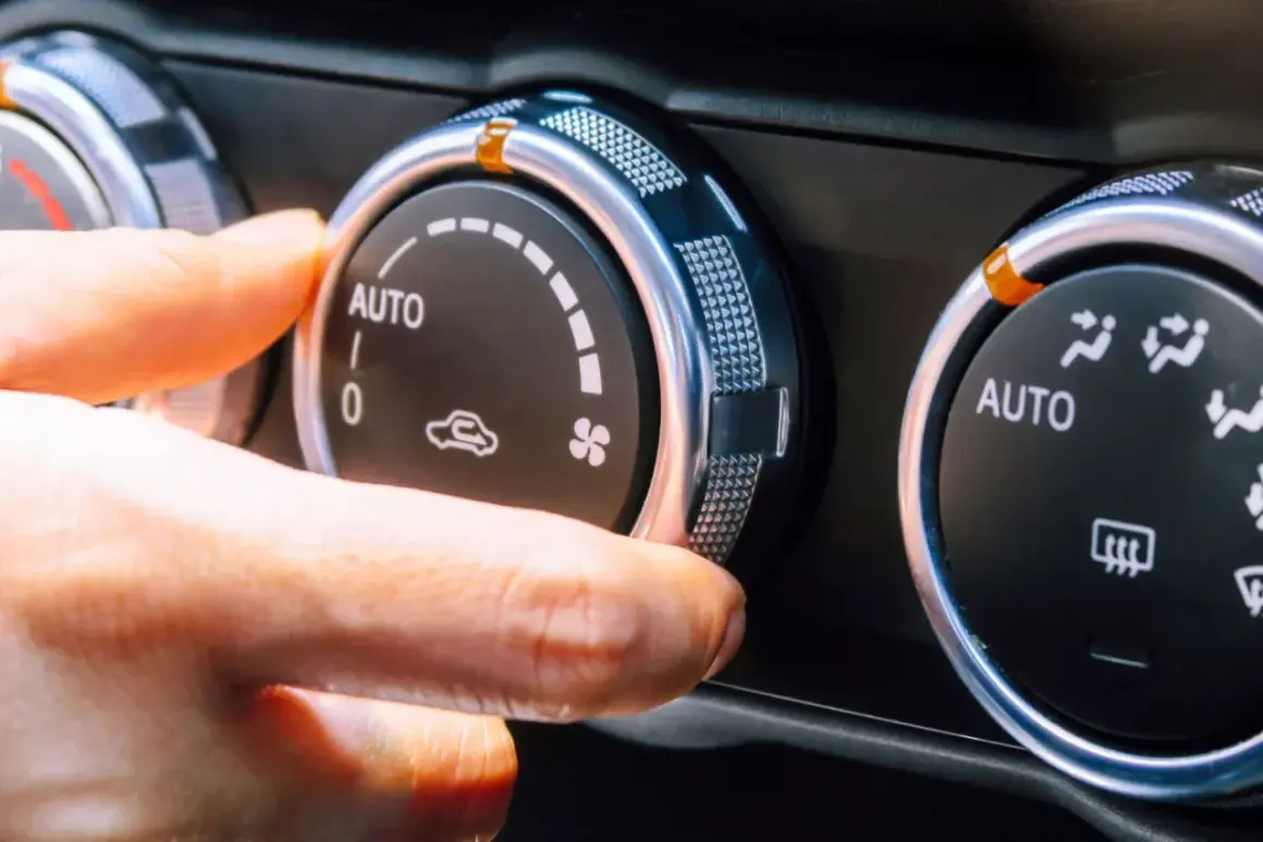 Dłoń reguluje pokrętło klimatyzacji w samochodzie, ustawiając tryb AUTO. Włączony jest czynnik chłodniczy, zapewniając komfortową temperaturę.