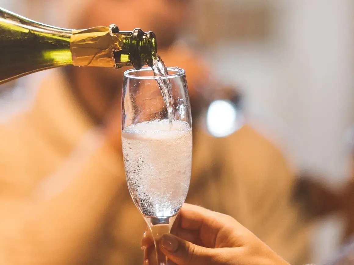 Schaumweine sorten: Ein Glas Sekt wird aus einer Flasche in ein Sektglas gegossen, das mit sprudelnden Bläschen gefüllt ist.