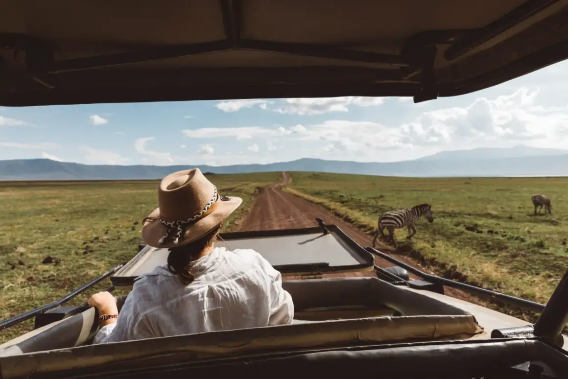 Mujer con sombrero en un safari en Tanzania, observando cebras en la sabana.