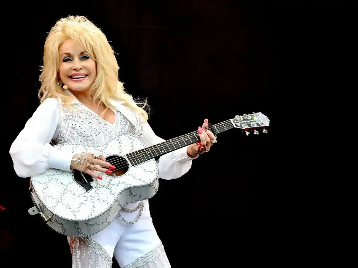 Dolly Parton, w białym, błyszczącym stroju, gra na gitarze. Wyobraź sobie, że śpiewa "Jolene", a tekst piosenki rozbrzmiewa w powietrzu.