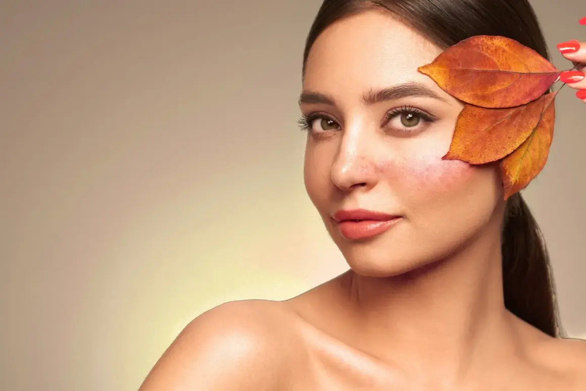 Une femme au teint légèrement rougi, cachant une partie de sa joue avec des feuilles d'automne. Une astuce pour savoir comment enlever des rougeurs rapidement.