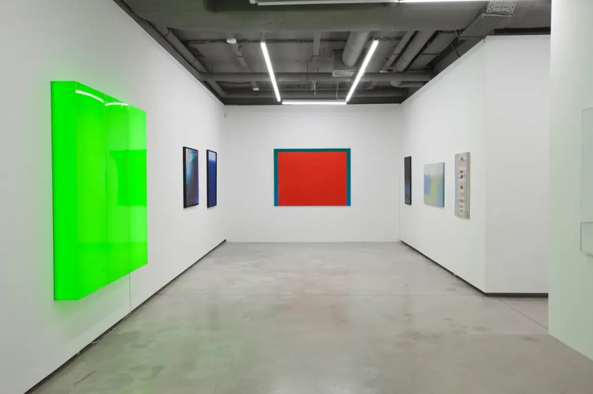 Galeria sztuki z neonowo-zieloną instalacją i obrazami, w tym dziełem Stefana Gierowskiego.