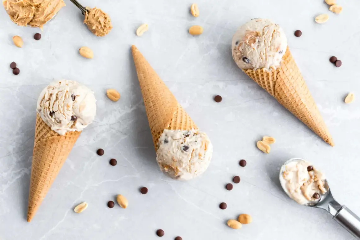 Drei Eiswaffeln mit cremigem Peanut Butter Cup Eis, umgeben von Erdnüssen und Schokostückchen.