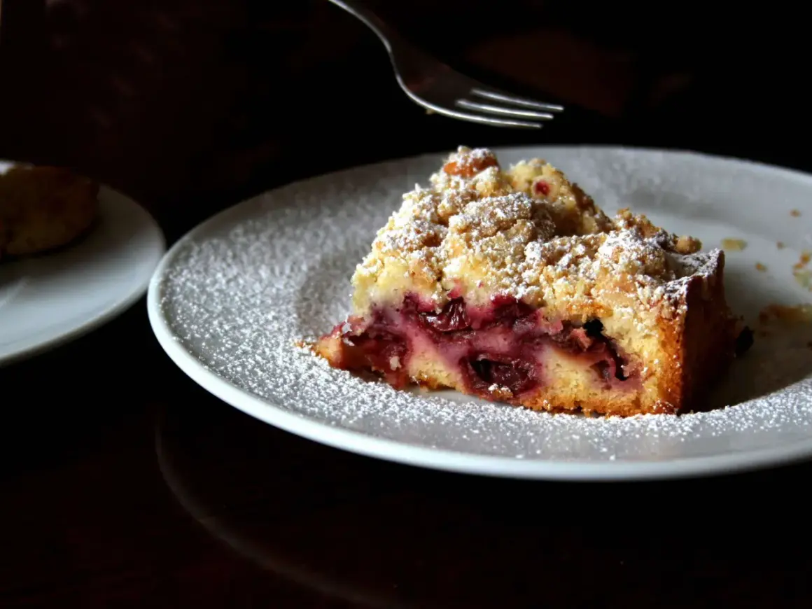 Ein Stück von Omas Kirschkuchen mit Streuseln, bestäubt mit Puderzucker, wartet auf seine Gabel.