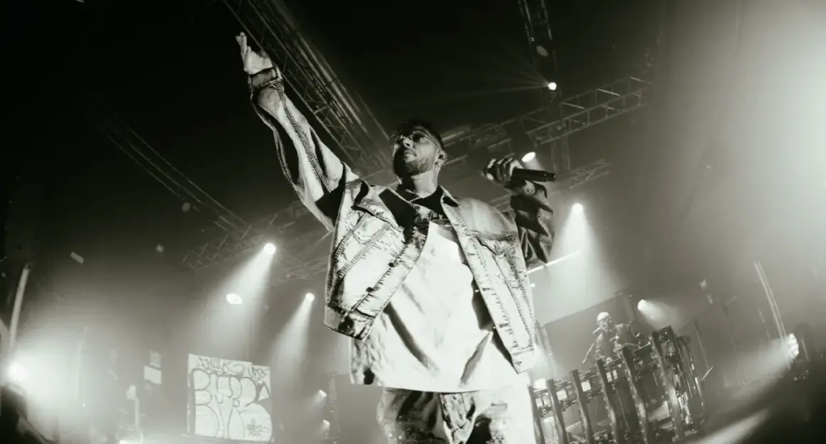 Emis Killa sul palco, con la mano alzata e il microfono in pugno, interpreta i suoi testi, parole di ghiaccio che riscaldano la folla.