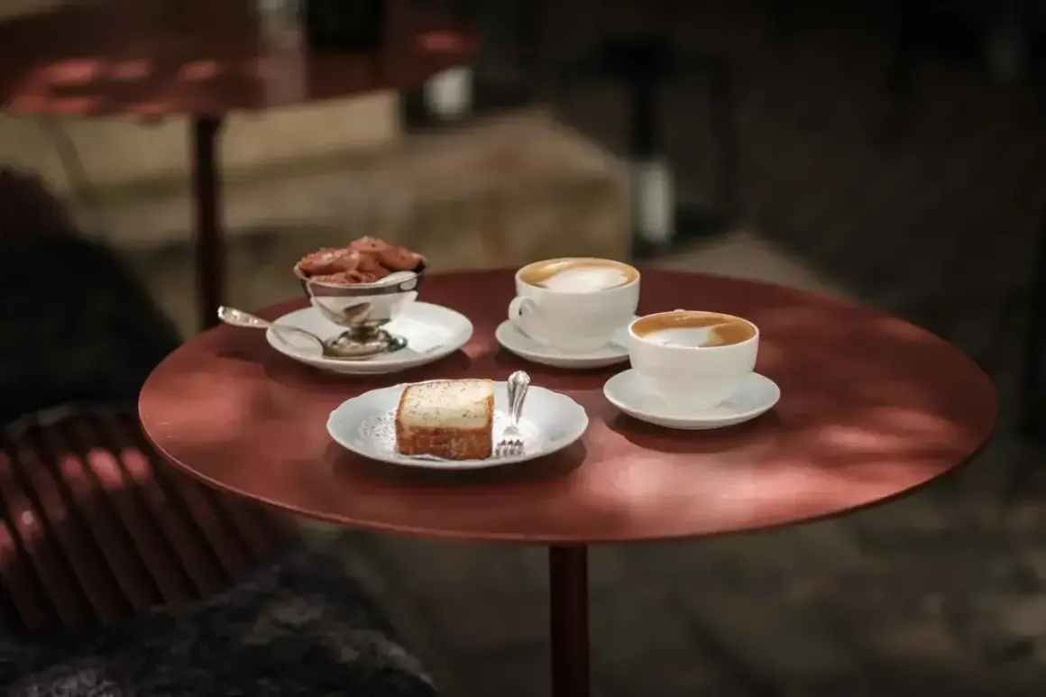Två kaffekoppar med latte macchiato och en latte står på ett rött bord. Bredvid finns en bit kaka och en skål med chokladmousse.