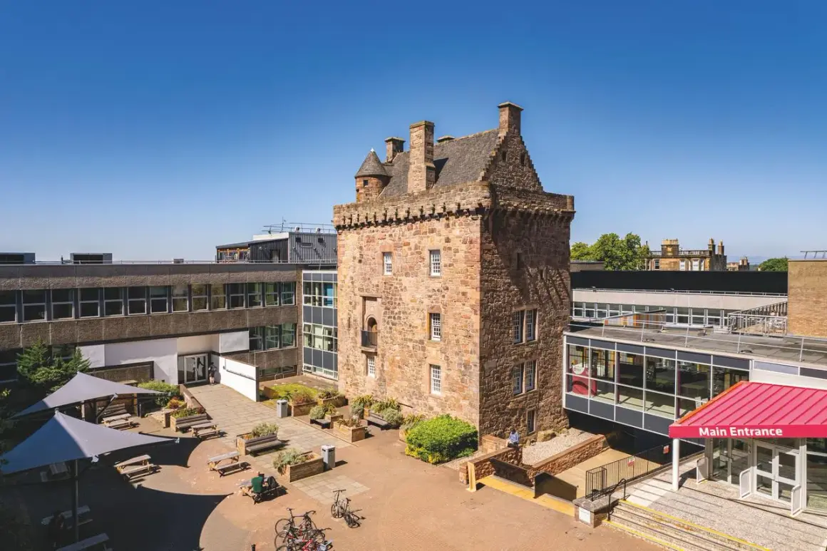 Historischer Turm des Edinburgh Napier Campus, umgeben von modernen Gebäuden und einem Innenhof mit Sitzgelegenheiten.