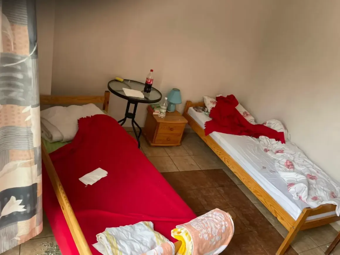 Pokój z dwoma łóżkami. Na jednym pościel po zmarłej osobie, przykryta czerwoną narzutą. Na drugim łóżku biała pościel z różowymi kwiatami i czerwony koc.