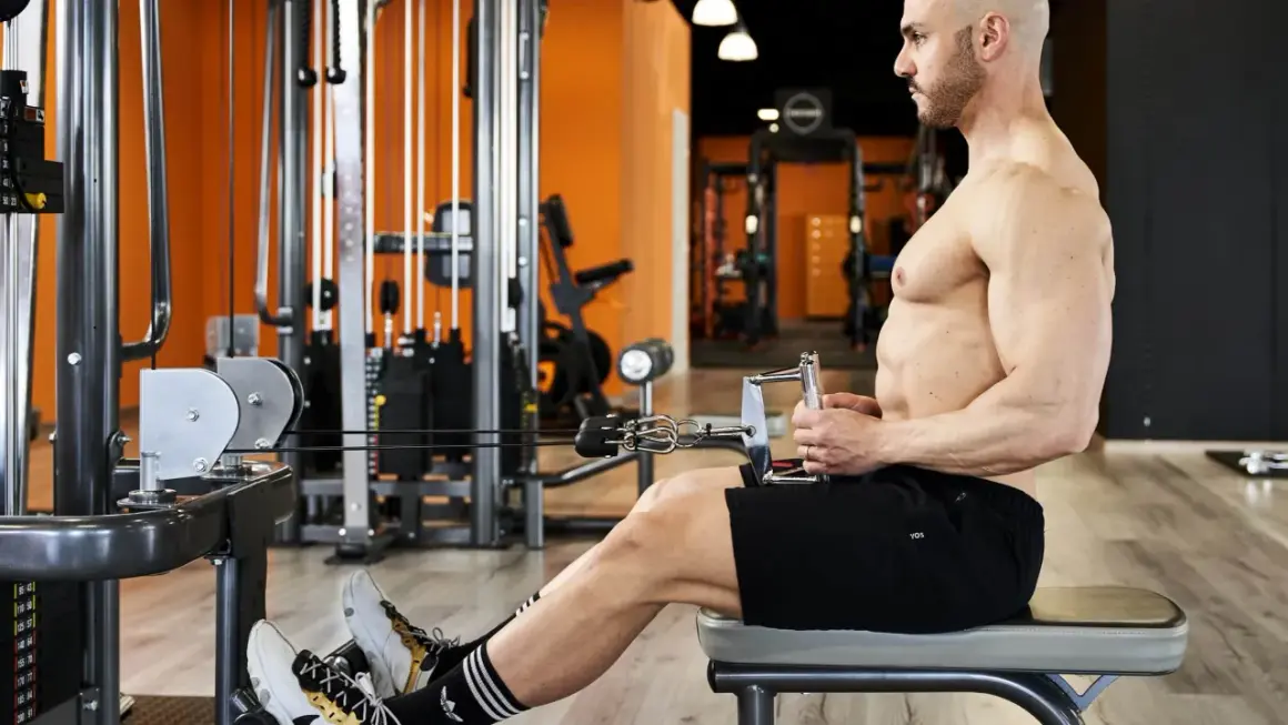 Uomo in palestra esegue un esercizio ai cavi, con le mani che afferrano la barra per le spinte in basso triangolo.