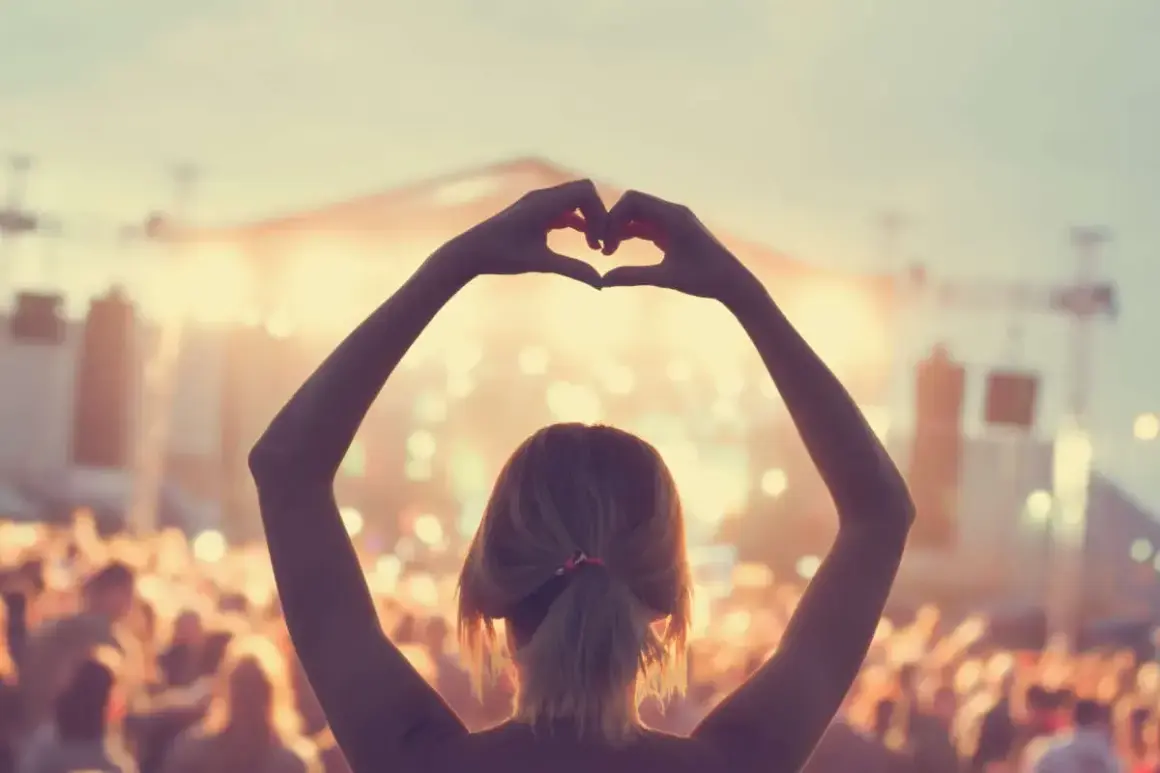 Ragazza fa un cuore con le mani a un concerto, immersa nell'atmosfera delle canzoni romantiche inglesi.