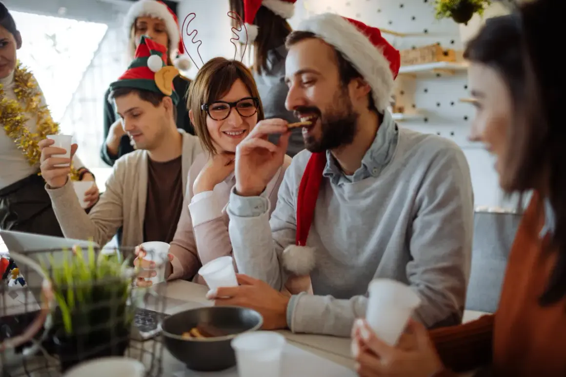 Fröhliche Menschen feiern Weihnachten. Sie tragen Weihnachtsmützen und trinken. Ist Heiligabend ein Feiertag? Ja, und sie genießen ihn!