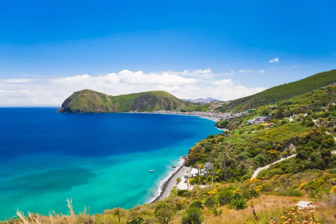Splendido mare di Lipari con acque cristalline che lambiscono una costa verdeggiante e un borgo bianco.